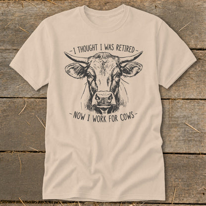 Light tan t-shirt with a sketch of a cow's head and text reading "I thought I was retired - now I work for cows."