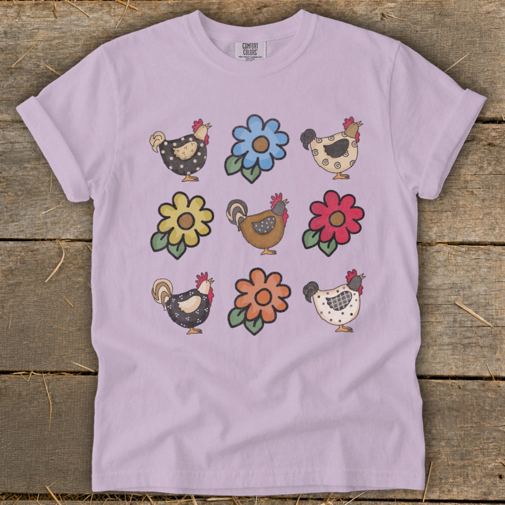 Lavender t-shirt with a grid of cartoon chickens and colorful flowers.