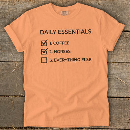 Orange t-shirt with black text: "DAILY ESSENTIALS 1. COFFEE 2. HORSES 3. EVERYTHING ELSE".