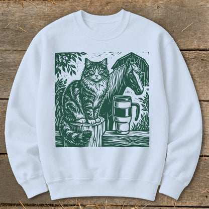 Green linocut print on white sweatshirt featuring a cat, horse, mug, and barn scene.