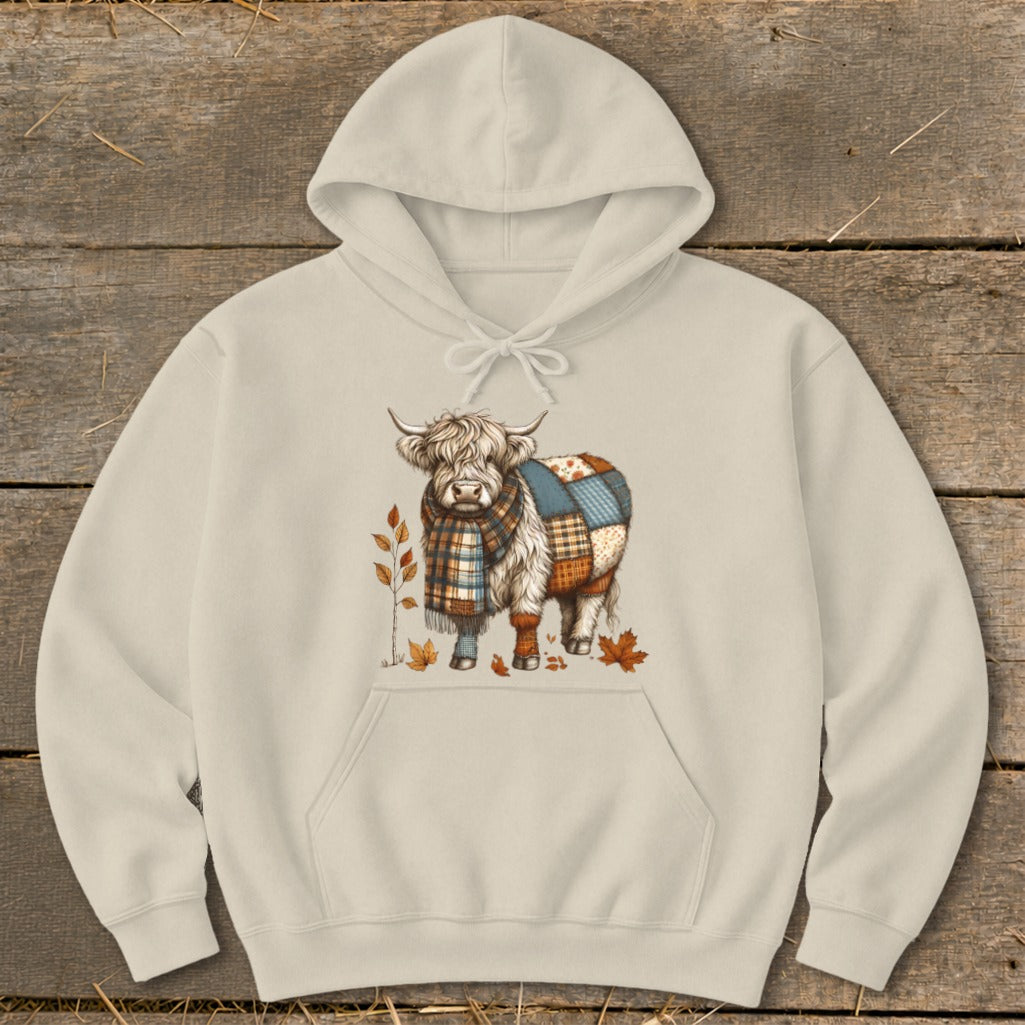 Cream hoodie with Highland cow graphic wearing a plaid scarf and patchwork blanket.