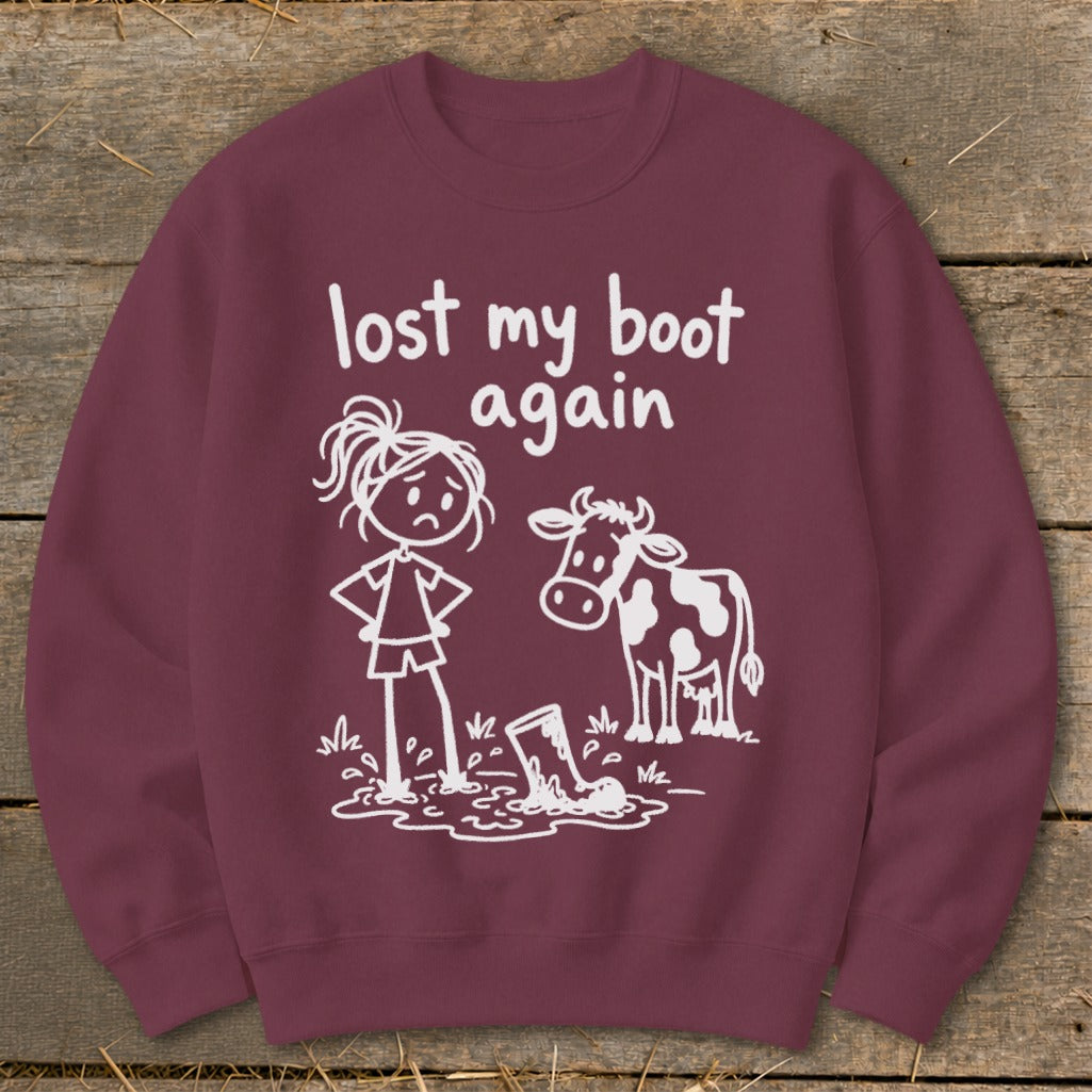 Maroon crewneck sweatshirt featuring white text that reads lost my boot again, alongside a drawing of a girl and a cow standing near a muddy boot.