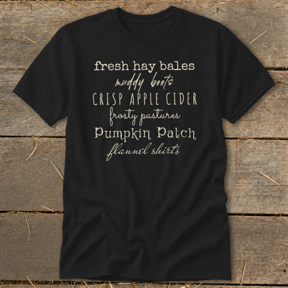 Black t-shirt with list of fall-themed phrases: fresh hay bales, muddy boots, crisp apple cider.