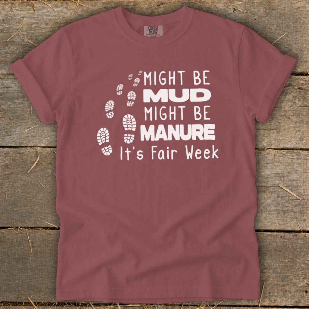 Maroon t-shirt with white text and boot prints that reads "Might Be Mud, Might Be Manure, It's Fair Week."