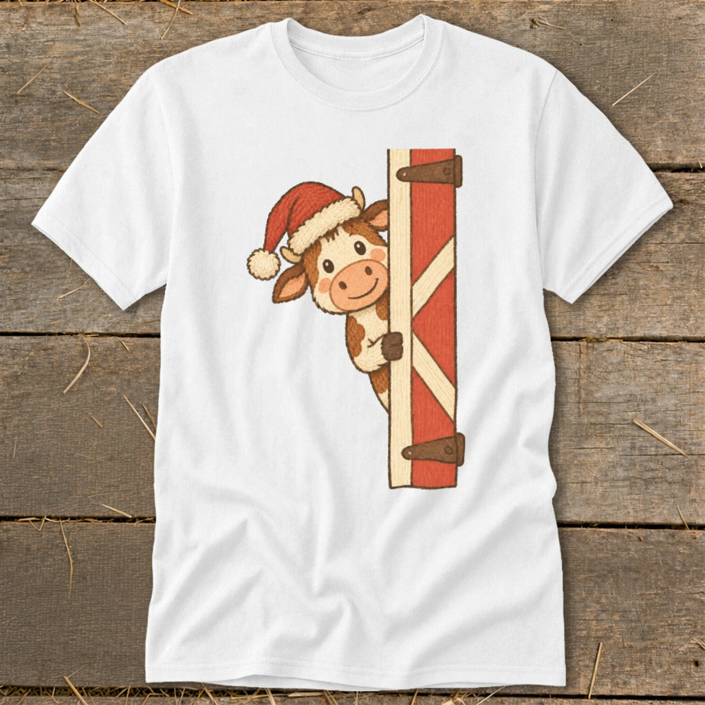 White t-shirt with a cartoon cow wearing a Santa hat peeking from behind a red barn door.