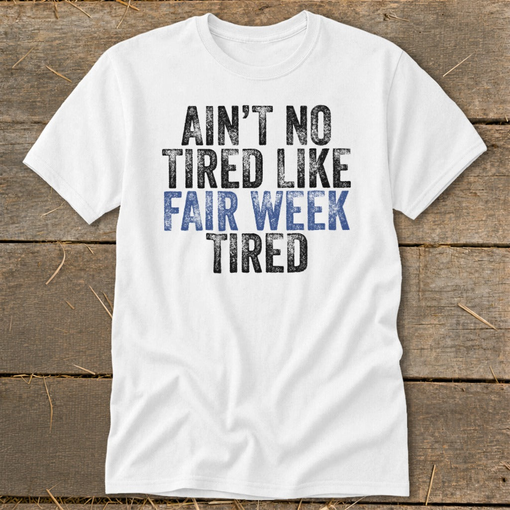 White t-shirt with black and blue text reading "Ain't no tired like fair week tired".