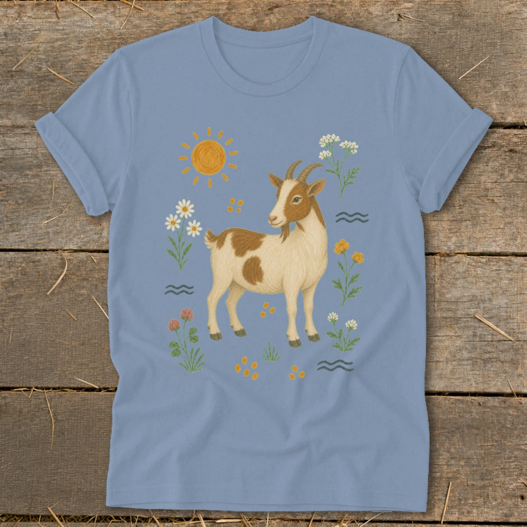 Illustration of a brown and white goat standing among flowers and a sun on a light blue t-shirt.
