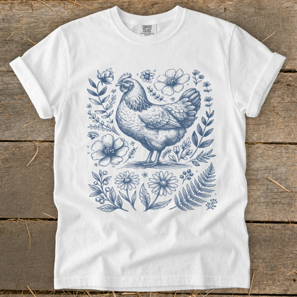 White t-shirt with a blue line drawing of a hen surrounded by flowers and foliage.