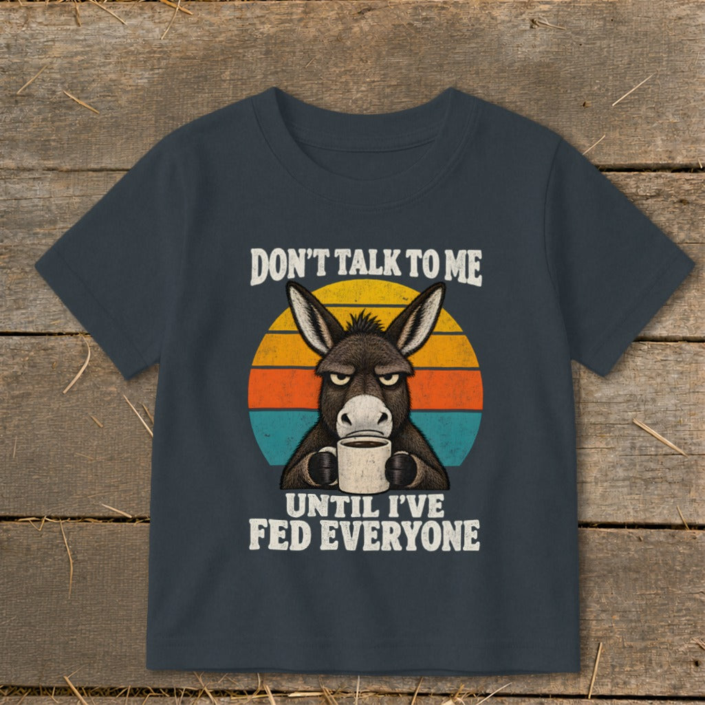Dark gray t-shirt with a vintage graphic of a grumpy donkey holding a coffee mug and text reading DON'T TALK TO ME UNTIL I'VE FED EVERYONE.