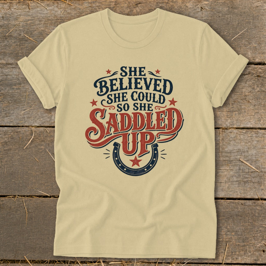 Light yellow t-shirt with "She believed she could so she saddled up" text and horseshoe graphic.