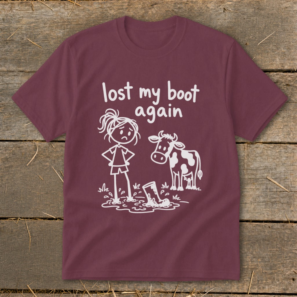 Maroon t-shirt featuring a white graphic of a frustrated stick figure girl next to a cow and a muddy boot, with the text lost my boot again.
