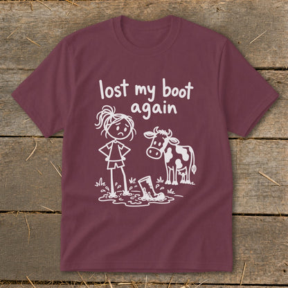 Maroon t-shirt featuring a white graphic of a frustrated stick figure girl next to a cow and a muddy boot, with the text lost my boot again.