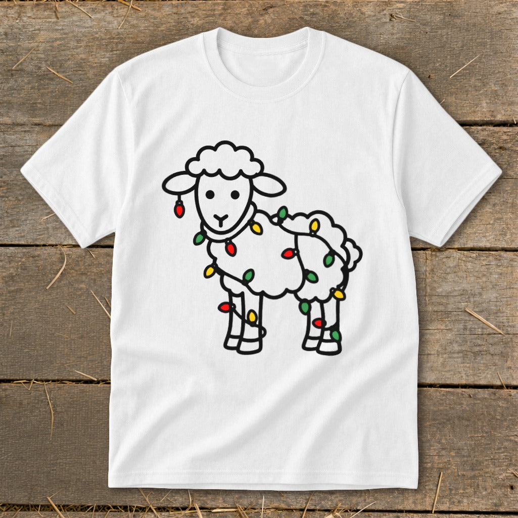 A white crewneck t-shirt featuring a line art illustration of a sheep tangled in Christmas lights, laid flat on a rustic wooden background.
