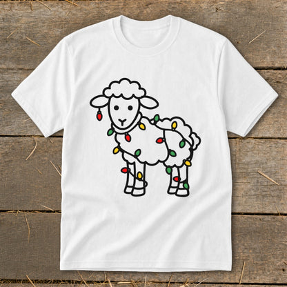 A white crewneck t-shirt featuring a line art illustration of a sheep tangled in Christmas lights, laid flat on a rustic wooden background.