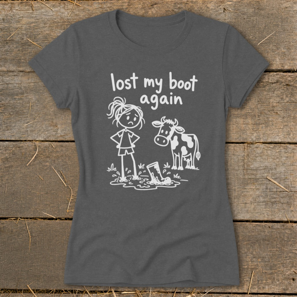 A dark gray t-shirt featuring a white graphic of a girl, a cow, and a boot stuck in mud with text saying lost my boot again.