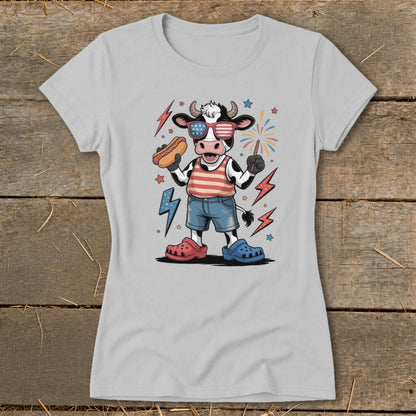 Cartoon cow wearing American flag sunglasses, holding a hot dog and sparkler with fireworks.
