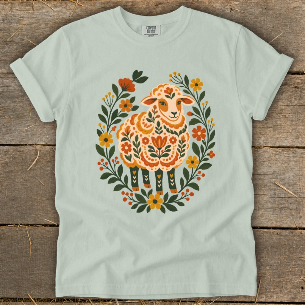Light green t-shirt with folk art sheep surrounded by flowers and leaves.
