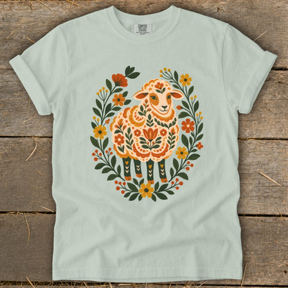 Light green t-shirt with folk art sheep surrounded by flowers and leaves.