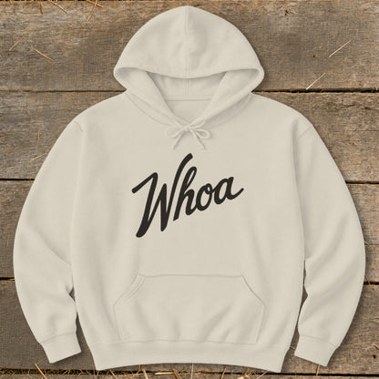 Cream hoodie with "Whoa" graphic on a wooden background.