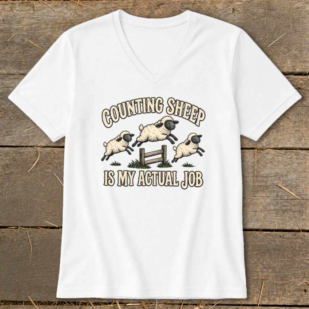 White t-shirt with "COUNTING SHEEP IS MY ACTUAL JOB" text and cartoon sheep jumping over a fence.