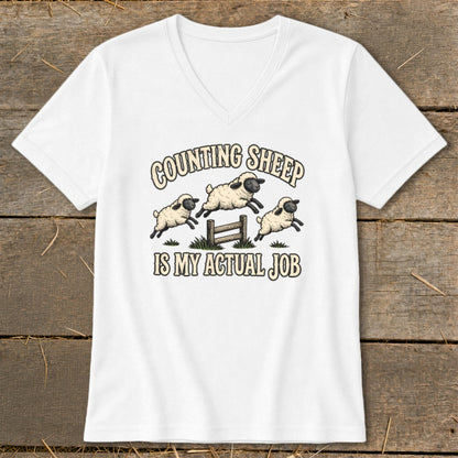 White t-shirt with "COUNTING SHEEP IS MY ACTUAL JOB" text and cartoon sheep jumping over a fence.