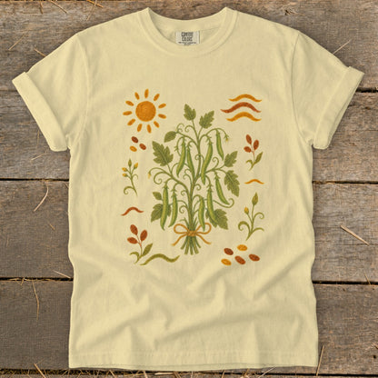 Light yellow t-shirt with a central illustration of a pea pod plant and a sun.