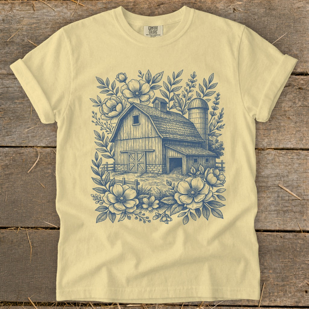 Light yellow t-shirt with a blue ink drawing of a barn surrounded by flowers.