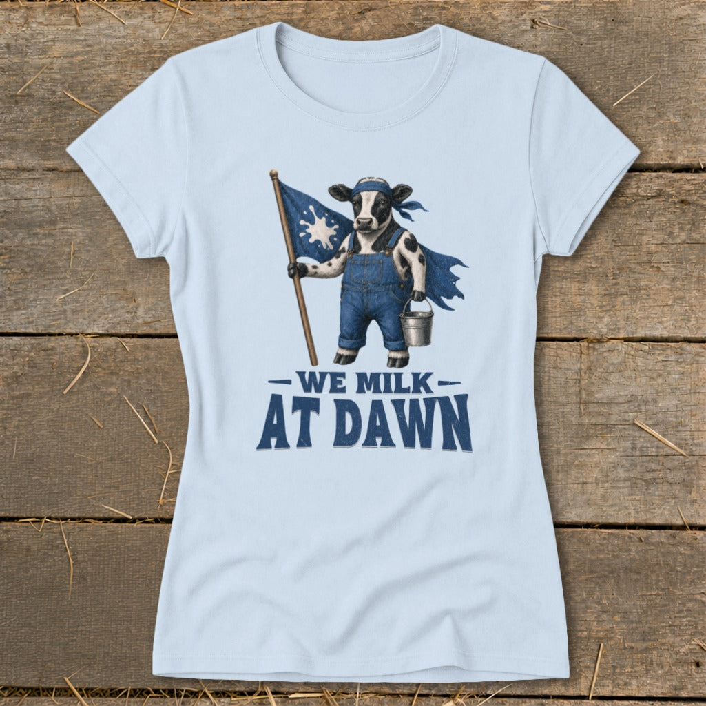 T-shirt with a cartoon cow in overalls, cape, and bucket, holding a flag with text "WE MILK AT DAWN".