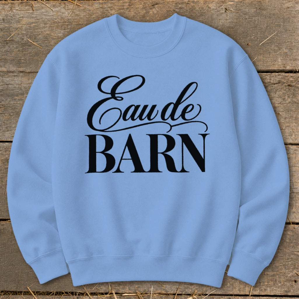 Light blue sweatshirt with black text "Eau de BARN" on a wooden background.