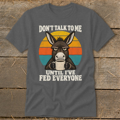 A dark gray t-shirt featuring an angry donkey holding a coffee mug with the text Don't Talk to Me Until I've Fed Everyone.