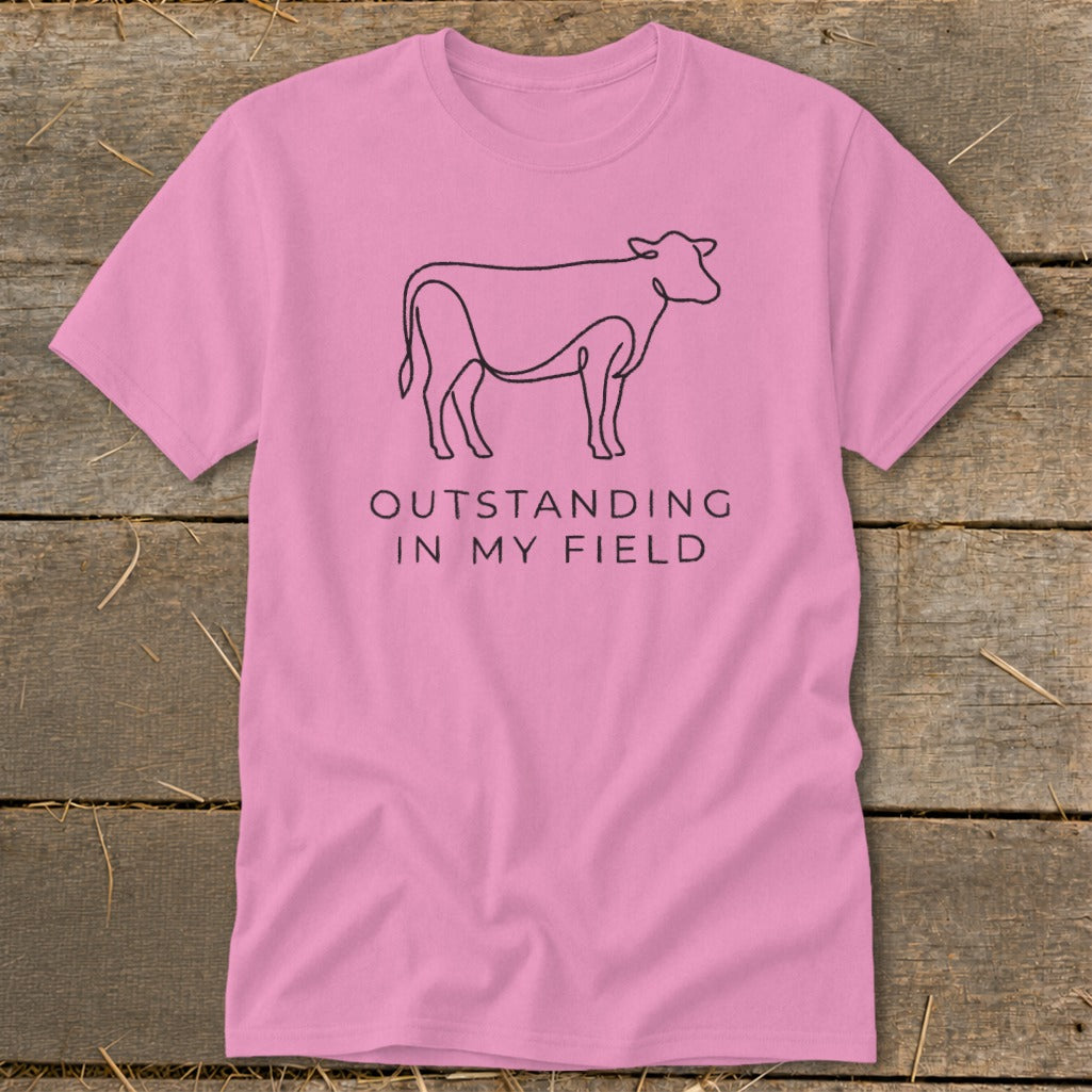 Pink t-shirt with black outline cow and text "OUTSTANDING IN MY FIELD".