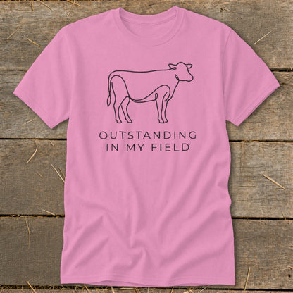 Pink t-shirt with black outline cow and text "OUTSTANDING IN MY FIELD".
