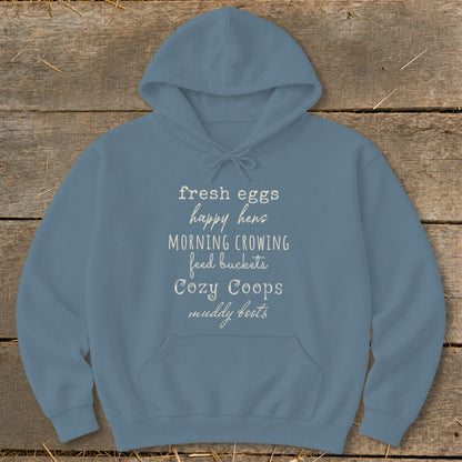 Blue hoodie with text listing: fresh eggs, happy hens, morning crowing, feed buckets, cozy coops, muddy boots.