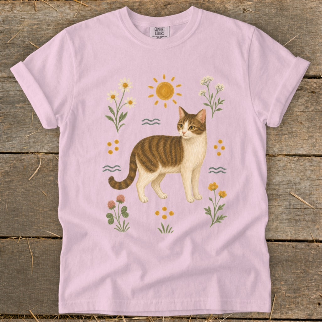 Pink t-shirt with tabby cat, sun, flowers, and clover graphic.