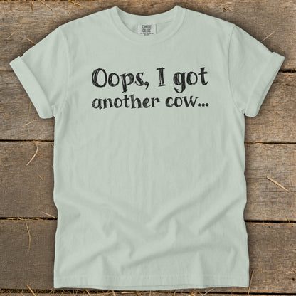 Light green t-shirt with black text reading "Oops, I got another cow...".