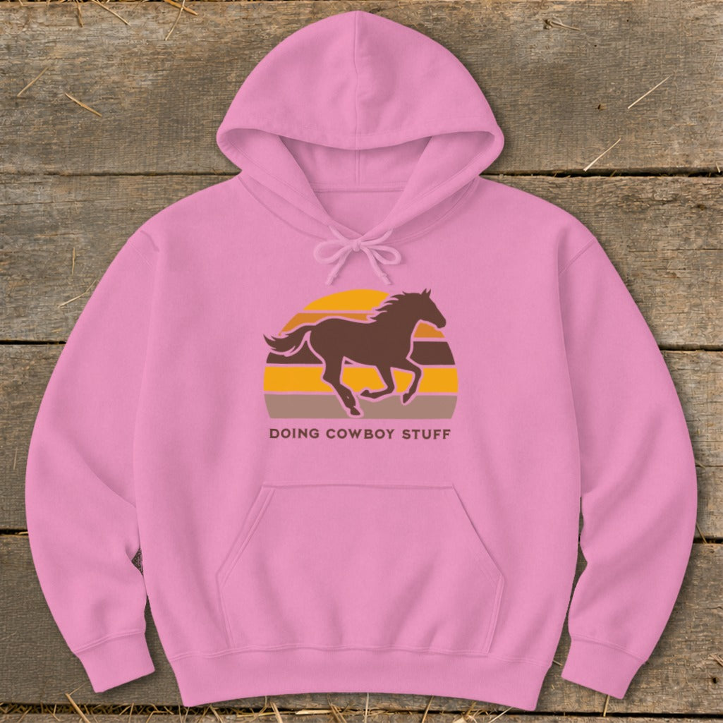 Pink hoodie with a brown horse silhouette over a striped sunset and the text "DOING COWBOY STUFF".