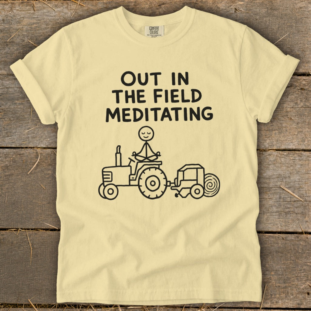 Yellow t-shirt with text "OUT IN THE FIELD MEDITATING" and a stick figure meditating on a tractor.