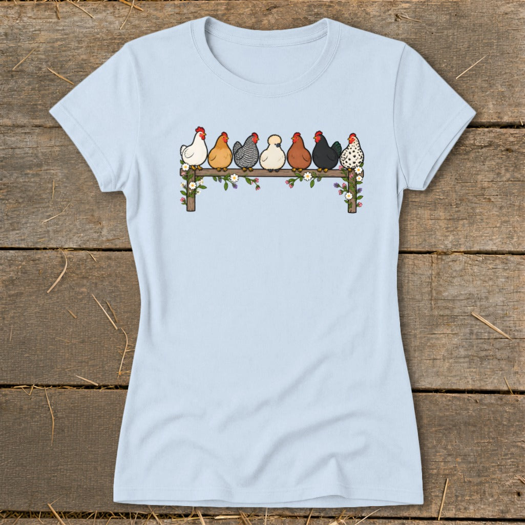 Light blue women's t-shirt featuring an illustration of seven colorful chickens perched on a flower-decorated fence.