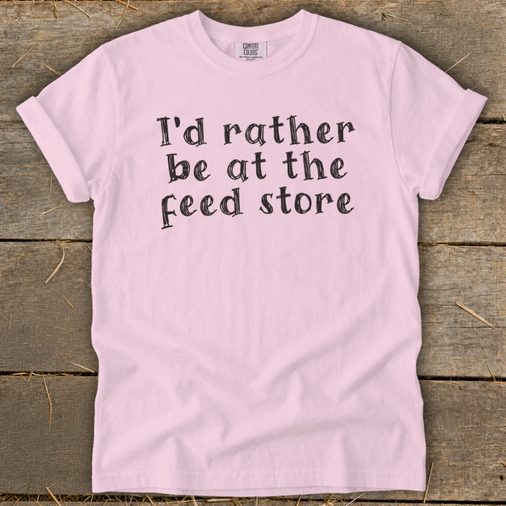 Pink t-shirt with black text that reads "I'd rather be at the feed store."