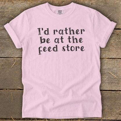 Pink t-shirt with black text that reads "I'd rather be at the feed store."