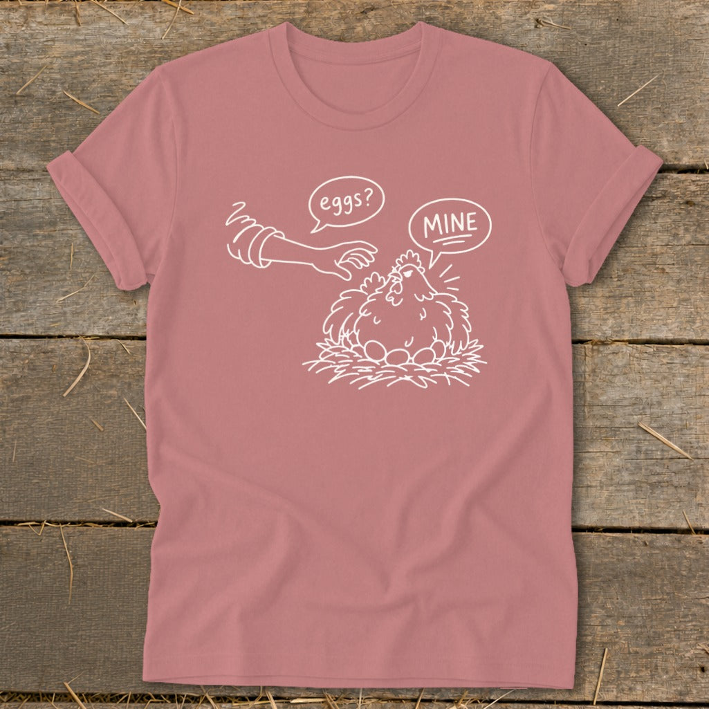 Pink t-shirt with white illustration of a chicken protecting eggs, saying "MINE".