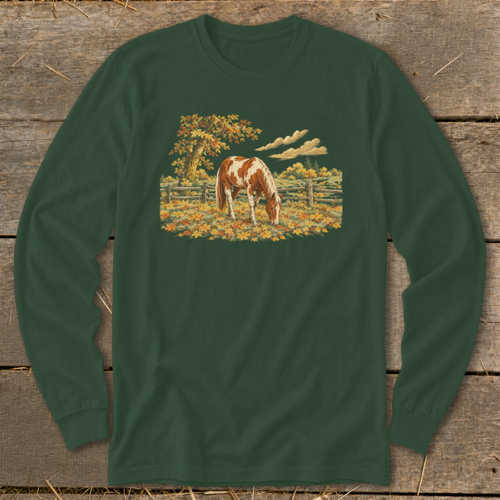 Brown and white horse grazing in a field of autumn leaves near a wooden fence.