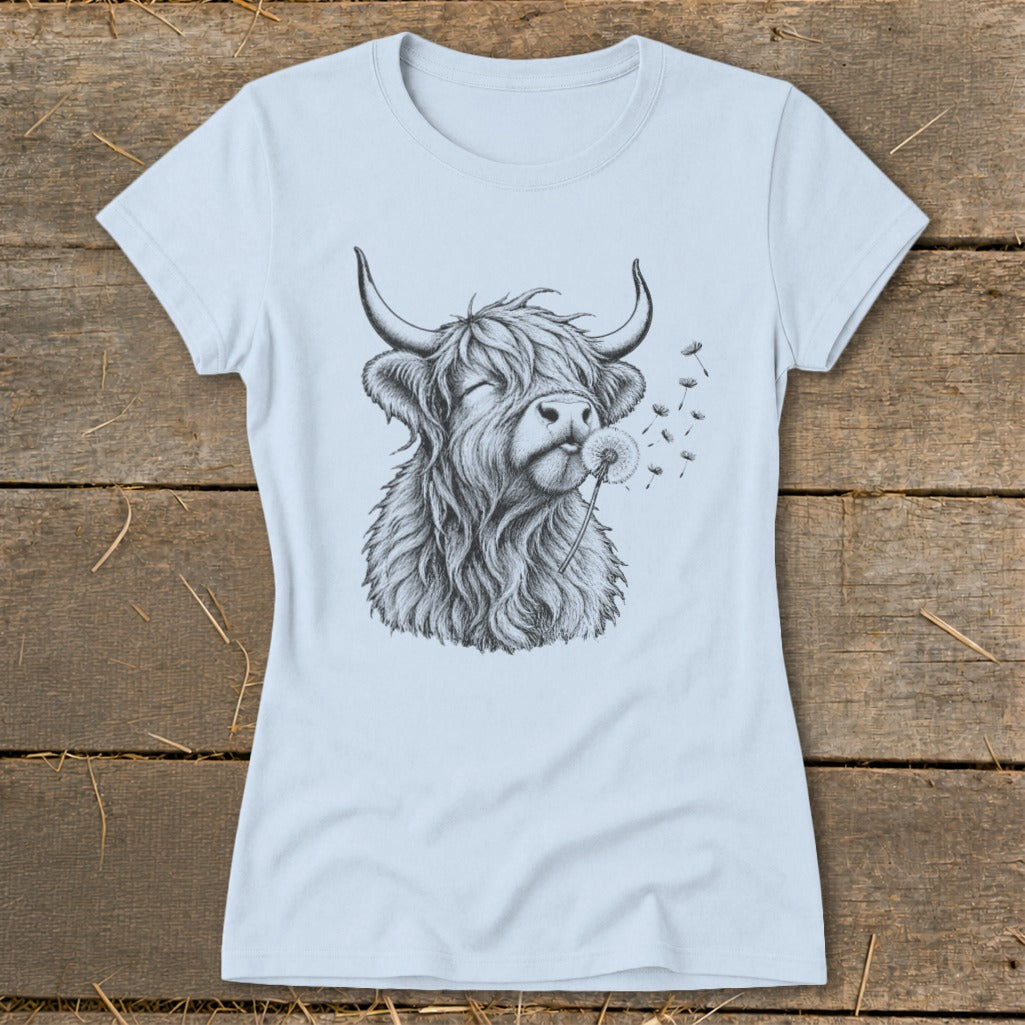 Black and white sketch of a highland cow blowing a dandelion on a light blue t-shirt.
