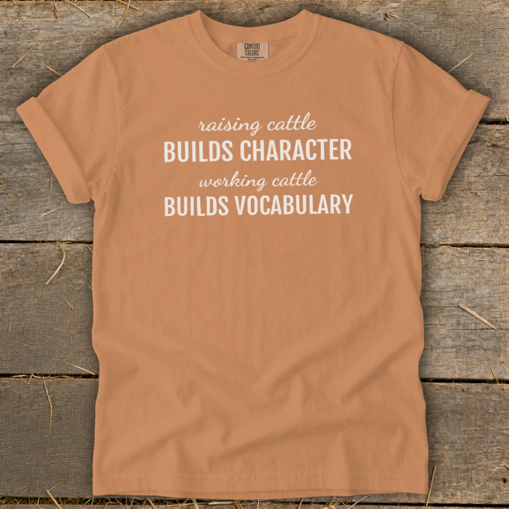 Orange t-shirt with white text: "raising cattle BUILDS CHARACTER working cattle BUILDS VOCABULARY"
