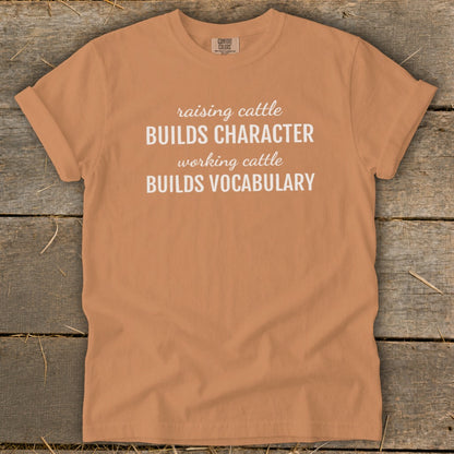 Orange t-shirt with white text: "raising cattle BUILDS CHARACTER working cattle BUILDS VOCABULARY"