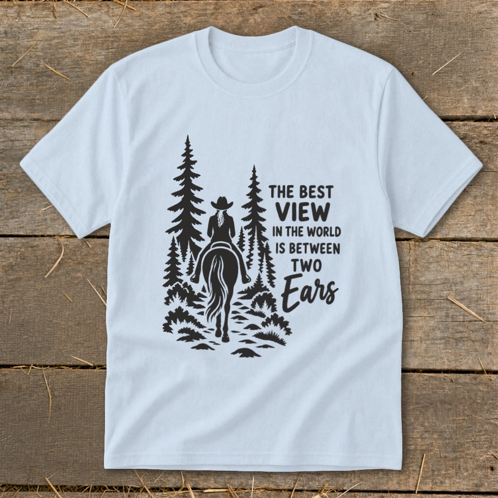 A light blue crewneck t-shirt featuring a black silhouette graphic of a horseback rider and pine trees with text that reads The Best View In The World Is Between Two Ears.