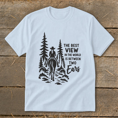 A light blue crewneck t-shirt featuring a black silhouette graphic of a horseback rider and pine trees with text that reads The Best View In The World Is Between Two Ears.