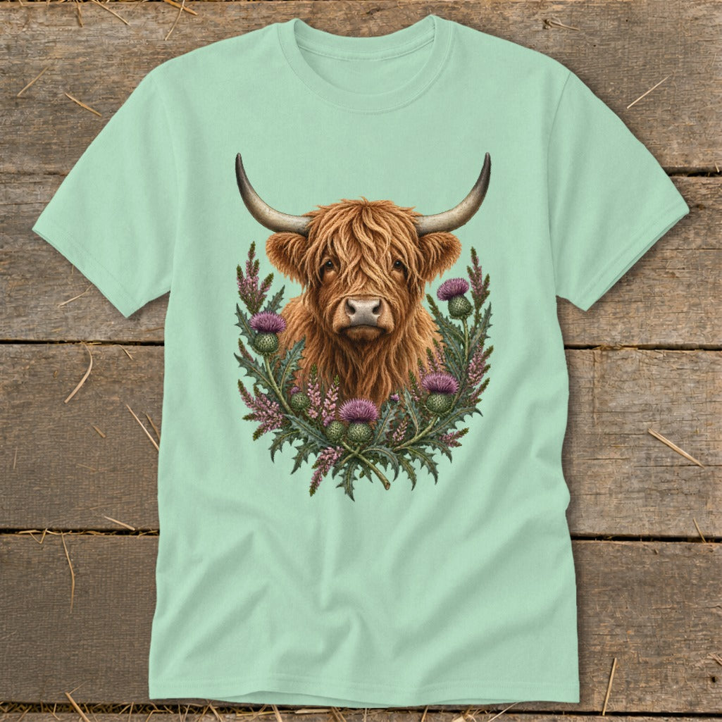 Highland cow with thistle wreath graphic on a light green t-shirt.