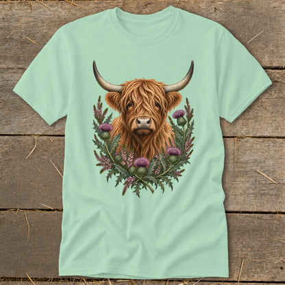 Highland cow with thistle wreath graphic on a light green t-shirt.