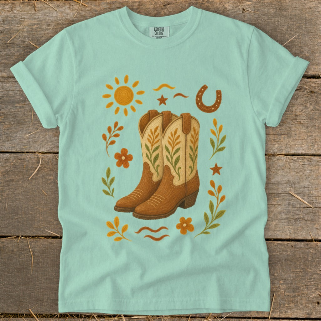 Light blue t-shirt with a western cowboy boot graphic and sun, horseshoe, and floral accents.